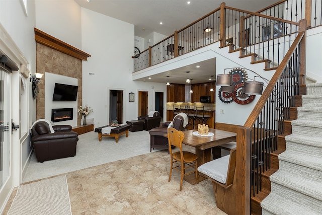 dining room with a towering ceiling, light carpet, and a tile fireplace