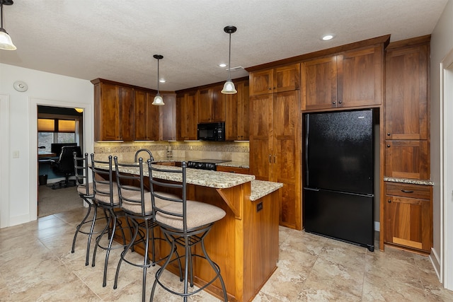 kitchen featuring light stone countertops, black appliances, decorative light fixtures, and an island with sink