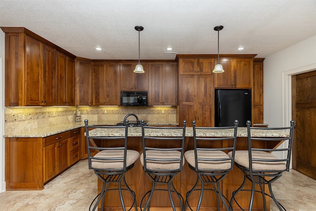 kitchen with light stone countertops, black appliances, a center island with sink, and pendant lighting