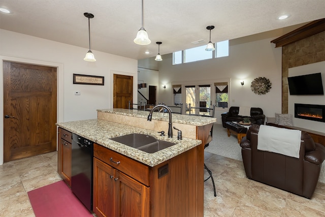 kitchen featuring black dishwasher, sink, an island with sink, a fireplace, and decorative light fixtures