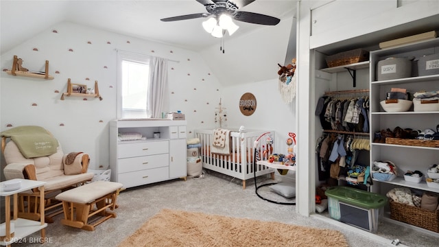 bedroom with ceiling fan, vaulted ceiling, a crib, a closet, and light colored carpet