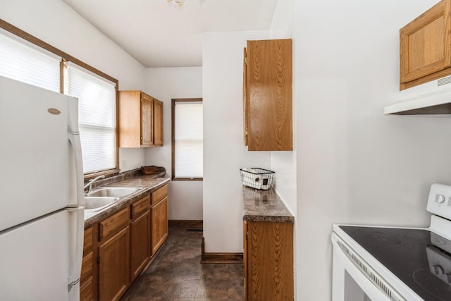 kitchen featuring white appliances, brown cabinetry, dark countertops, under cabinet range hood, and a sink