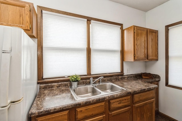 kitchen featuring dark countertops, a sink, freestanding refrigerator, and a healthy amount of sunlight