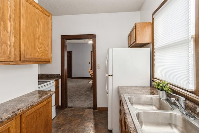 kitchen with dark countertops, a ceiling fan, a sink, white appliances, and baseboards