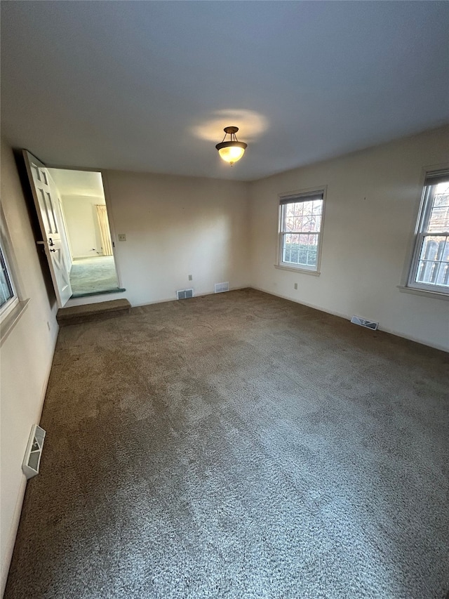 unfurnished room featuring a healthy amount of sunlight, carpet floors, and visible vents