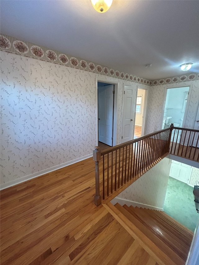 empty room with baseboards, wallpapered walls, and wood finished floors
