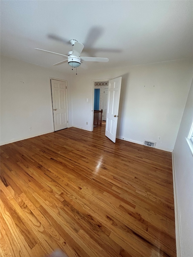 empty room with ceiling fan, wood finished floors, and visible vents