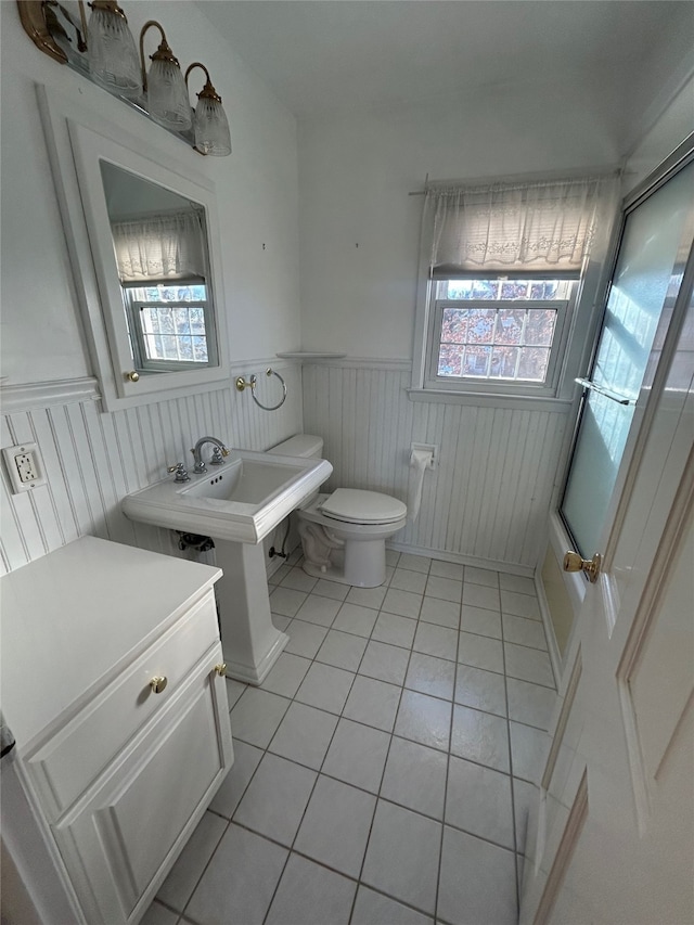 bathroom featuring toilet, tile patterned floors, a healthy amount of sunlight, and a wainscoted wall