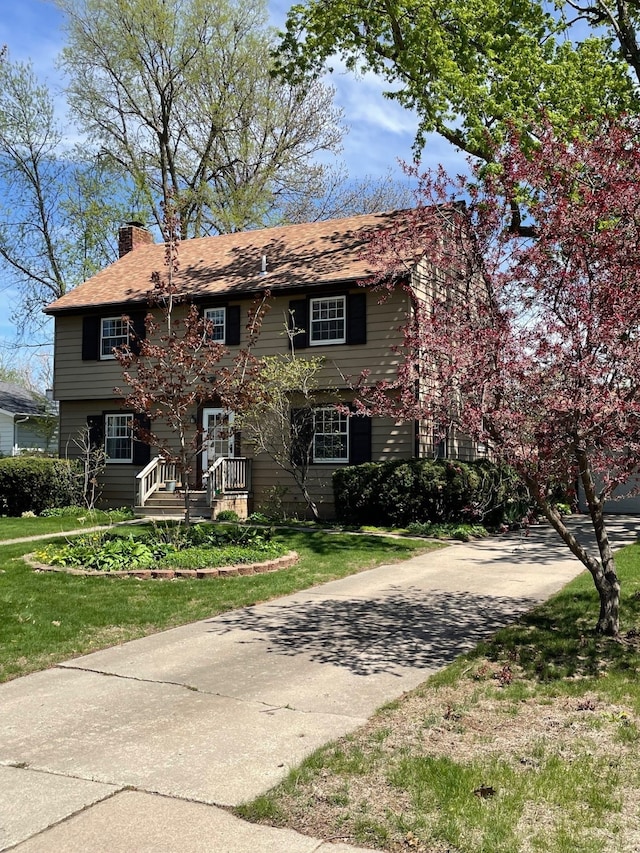 colonial home with a front lawn, driveway, and a chimney