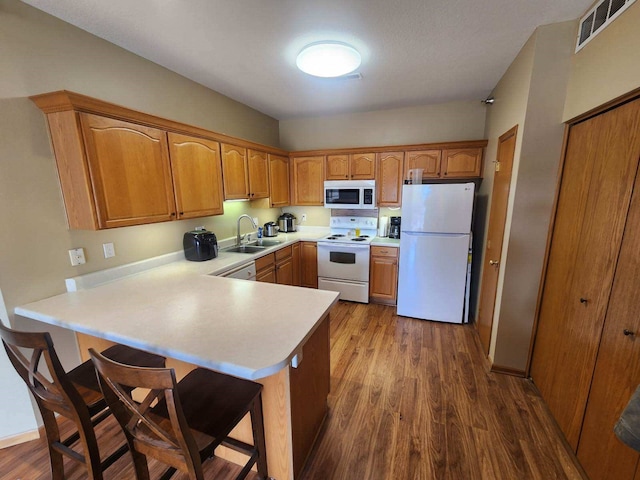 kitchen with white appliances, sink, kitchen peninsula, and dark hardwood / wood-style floors