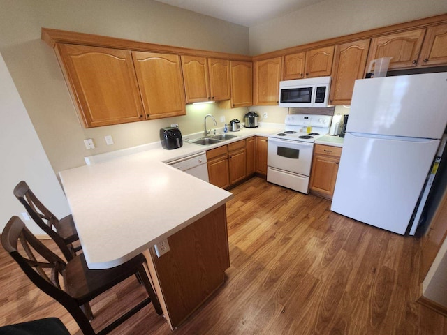 kitchen with light hardwood / wood-style flooring, kitchen peninsula, sink, a kitchen bar, and white appliances