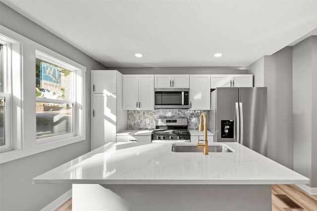 kitchen with sink, light stone countertops, white cabinets, appliances with stainless steel finishes, and light hardwood / wood-style floors