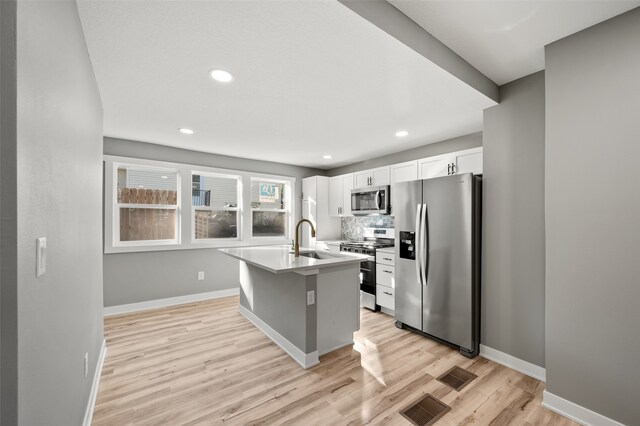 kitchen with appliances with stainless steel finishes, sink, white cabinets, light hardwood / wood-style flooring, and a kitchen island with sink