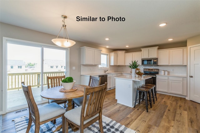 kitchen with decorative light fixtures, white cabinetry, stainless steel appliances, and light hardwood / wood-style flooring