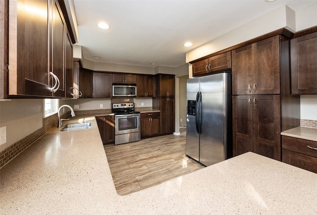 kitchen featuring appliances with stainless steel finishes, sink, dark brown cabinets, and light stone counters