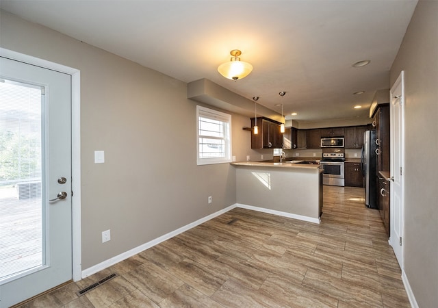 kitchen with kitchen peninsula, a breakfast bar area, appliances with stainless steel finishes, dark brown cabinetry, and sink