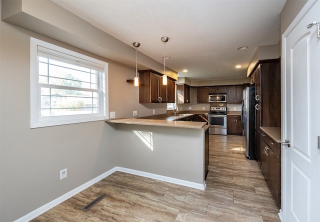 kitchen featuring kitchen peninsula, dark brown cabinets, hanging light fixtures, a breakfast bar area, and appliances with stainless steel finishes