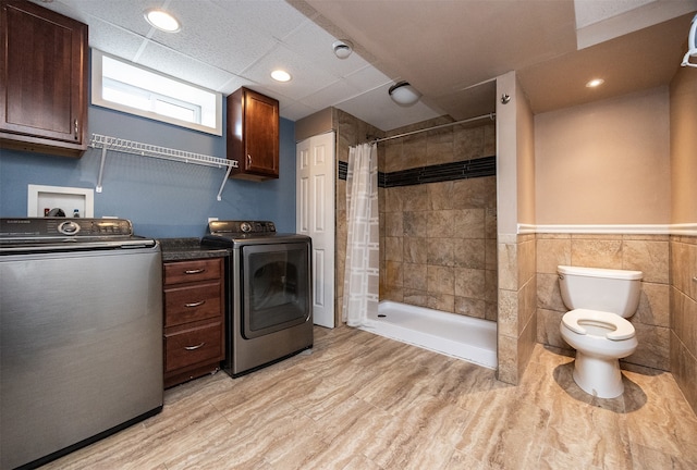 laundry room with light wood-type flooring, tile walls, and washing machine and clothes dryer