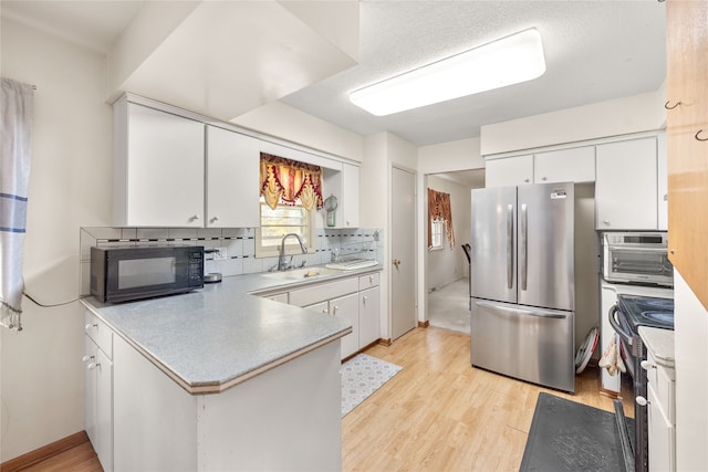 kitchen featuring black appliances, sink, light wood-type flooring, white cabinets, and decorative backsplash