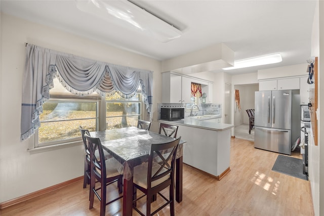 kitchen with kitchen peninsula, stainless steel fridge, white cabinets, light hardwood / wood-style flooring, and sink