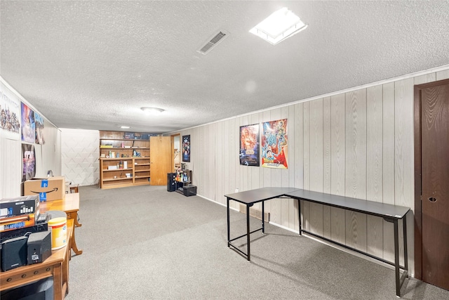 recreation room with built in features, wood walls, a textured ceiling, and carpet