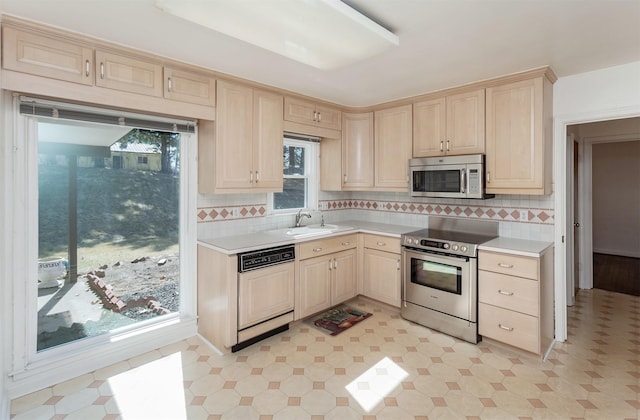 kitchen with tasteful backsplash, light brown cabinetry, light countertops, stainless steel appliances, and a sink