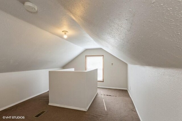 bonus room featuring dark colored carpet, a textured ceiling, and lofted ceiling