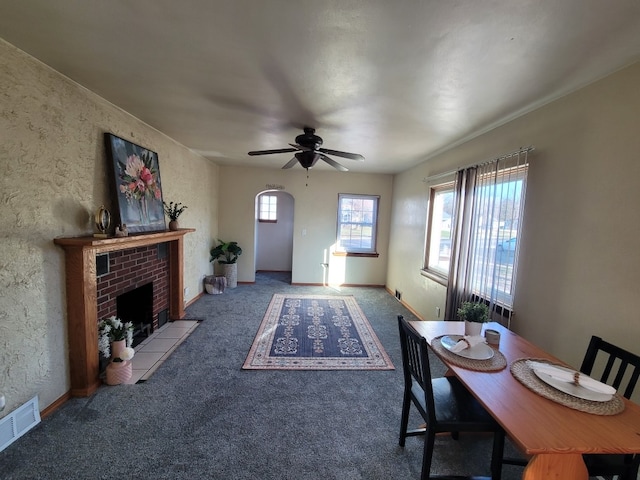 carpeted dining space with a brick fireplace and ceiling fan