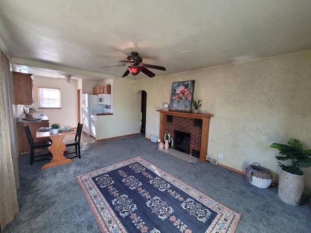 living room featuring dark colored carpet, ceiling fan, and a brick fireplace