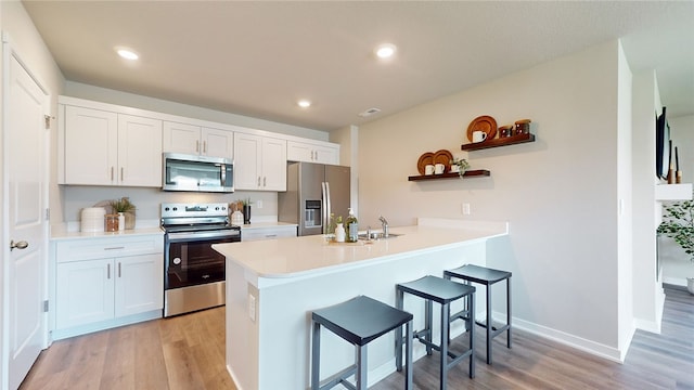 kitchen with a breakfast bar, kitchen peninsula, stainless steel appliances, light hardwood / wood-style floors, and white cabinets