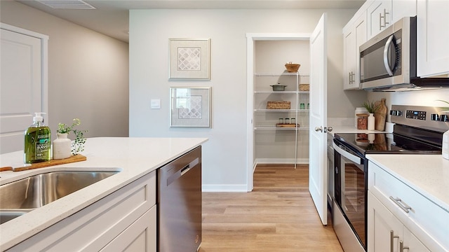 kitchen with stainless steel appliances, white cabinetry, sink, and light hardwood / wood-style floors