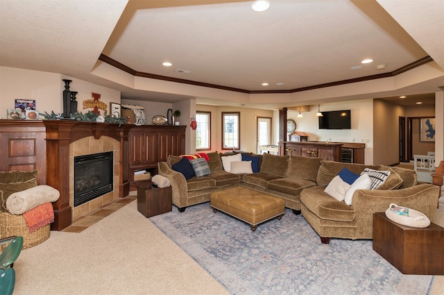 carpeted living room with a raised ceiling, crown molding, and a tiled fireplace