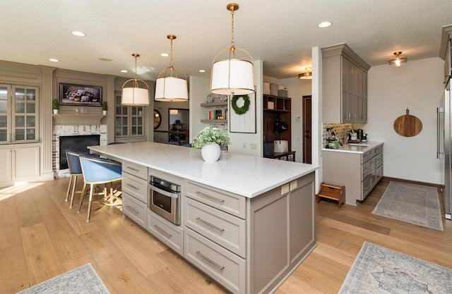 kitchen with pendant lighting, gray cabinetry, stainless steel oven, a spacious island, and a fireplace