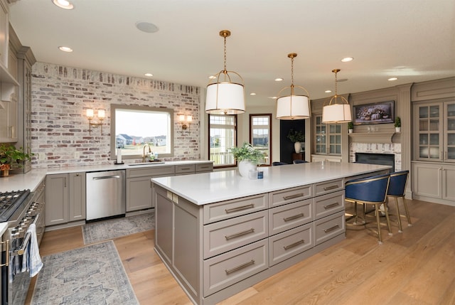 kitchen with sink, hanging light fixtures, brick wall, a kitchen island, and appliances with stainless steel finishes