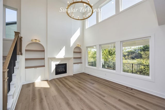 unfurnished living room featuring an inviting chandelier, a high ceiling, hardwood / wood-style flooring, and built in features