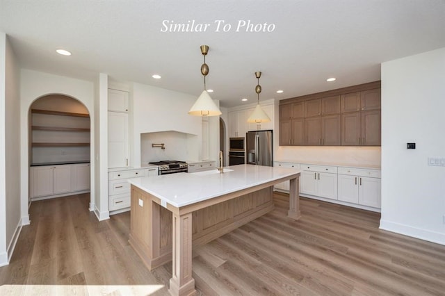 kitchen featuring appliances with stainless steel finishes, a large island, light hardwood / wood-style floors, white cabinetry, and pendant lighting