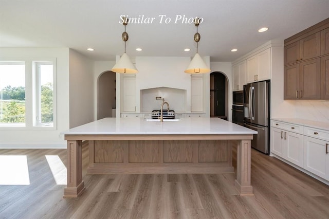 kitchen featuring appliances with stainless steel finishes, white cabinets, hanging light fixtures, and a large island with sink