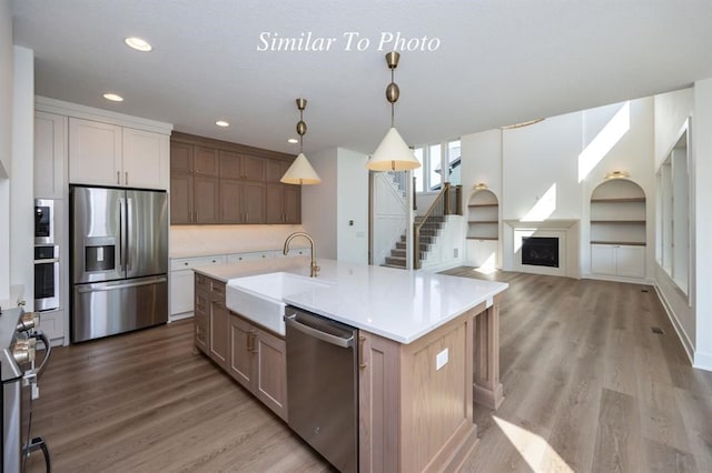 kitchen featuring hanging light fixtures, a spacious island, light wood-type flooring, stainless steel appliances, and sink