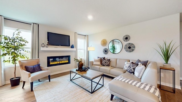 living room featuring baseboards, a glass covered fireplace, and wood finished floors