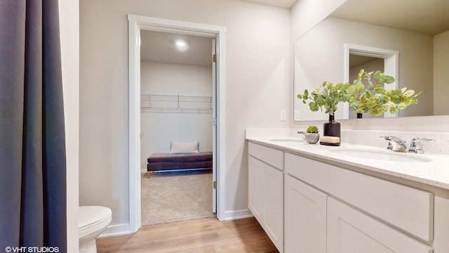 full bath with a sink, toilet, wood finished floors, and a spacious closet