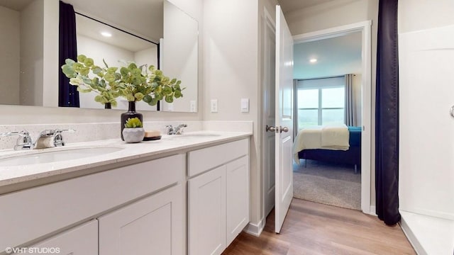 ensuite bathroom featuring double vanity, a sink, ensuite bath, and wood finished floors