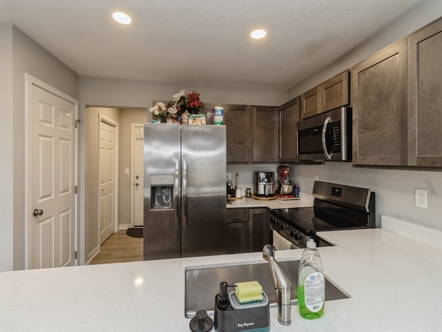 kitchen with dark brown cabinetry, stainless steel appliances, wood-type flooring, and sink