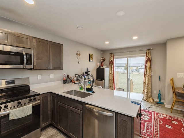 kitchen featuring kitchen peninsula, sink, dark brown cabinetry, appliances with stainless steel finishes, and light hardwood / wood-style floors