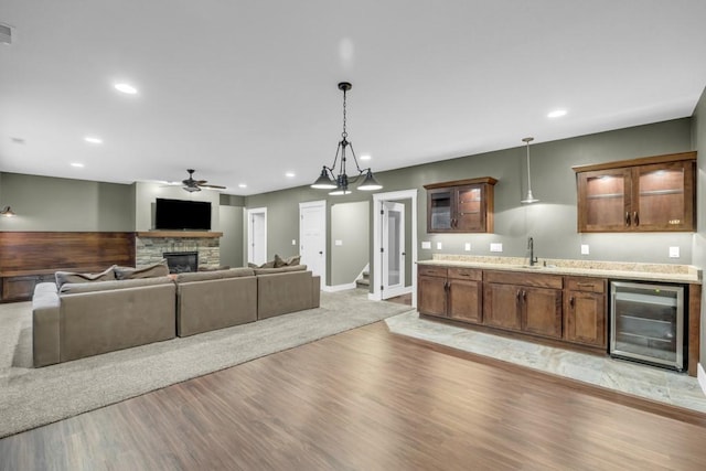 living room featuring a stone fireplace, wine cooler, ceiling fan, light hardwood / wood-style floors, and wet bar