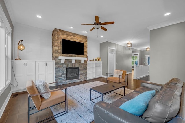 living room featuring hardwood / wood-style flooring, ornamental molding, a stone fireplace, and ceiling fan