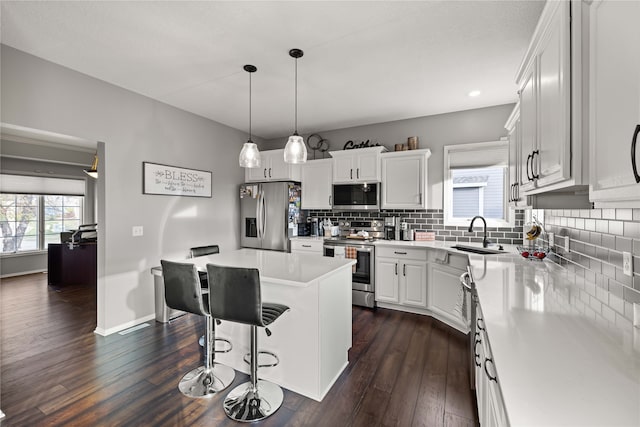 kitchen with appliances with stainless steel finishes, sink, a kitchen island, white cabinets, and dark wood-type flooring