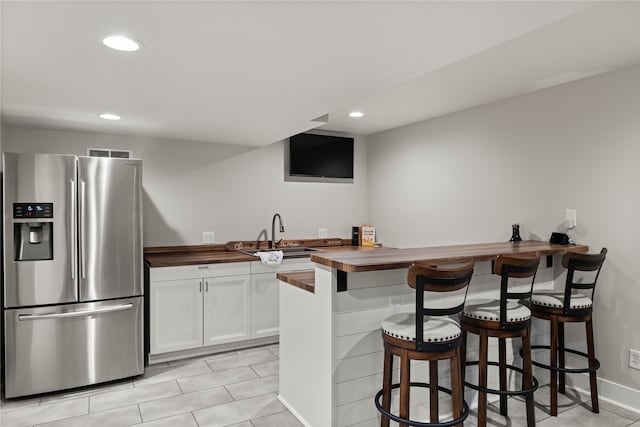 kitchen featuring butcher block counters, sink, stainless steel fridge with ice dispenser, a breakfast bar, and white cabinetry