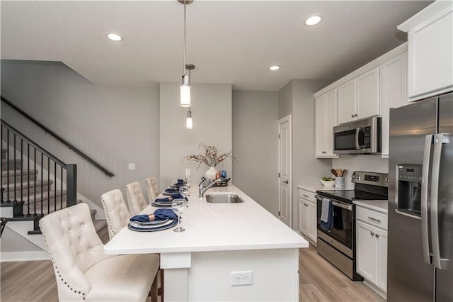 kitchen featuring appliances with stainless steel finishes, sink, decorative light fixtures, a breakfast bar, and a center island with sink