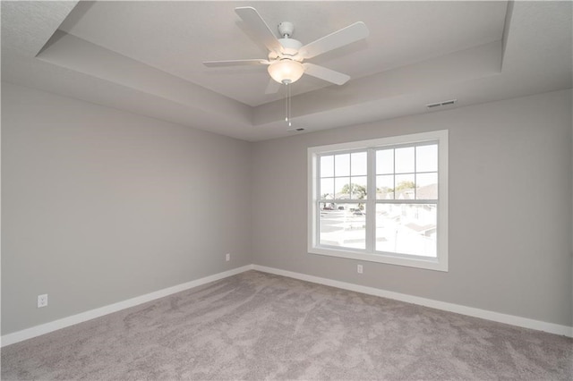 carpeted spare room with ceiling fan and a raised ceiling