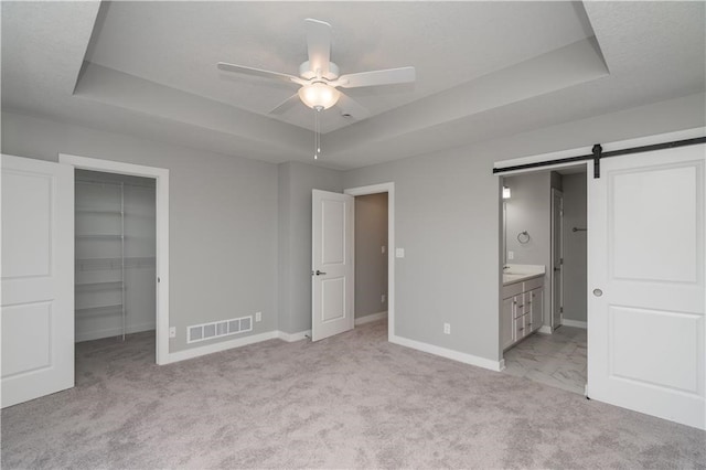 unfurnished bedroom featuring a walk in closet, a barn door, a tray ceiling, and ceiling fan